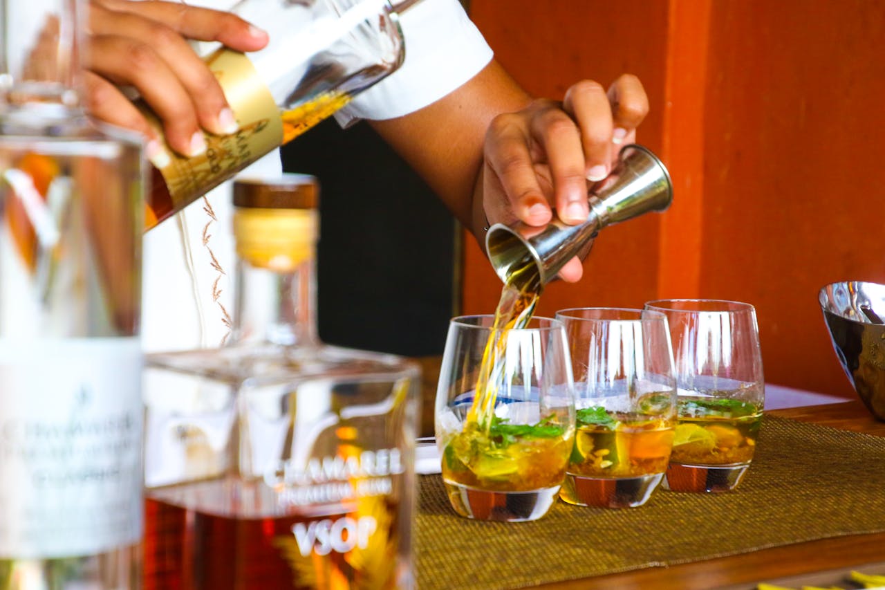 A bartender expertly pours cocktails in glasses on a bar counter.