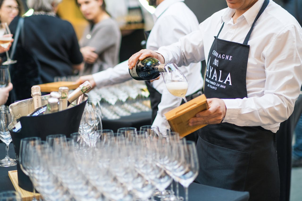 Server pouring champagne into glasses at an elegant indoor gathering.